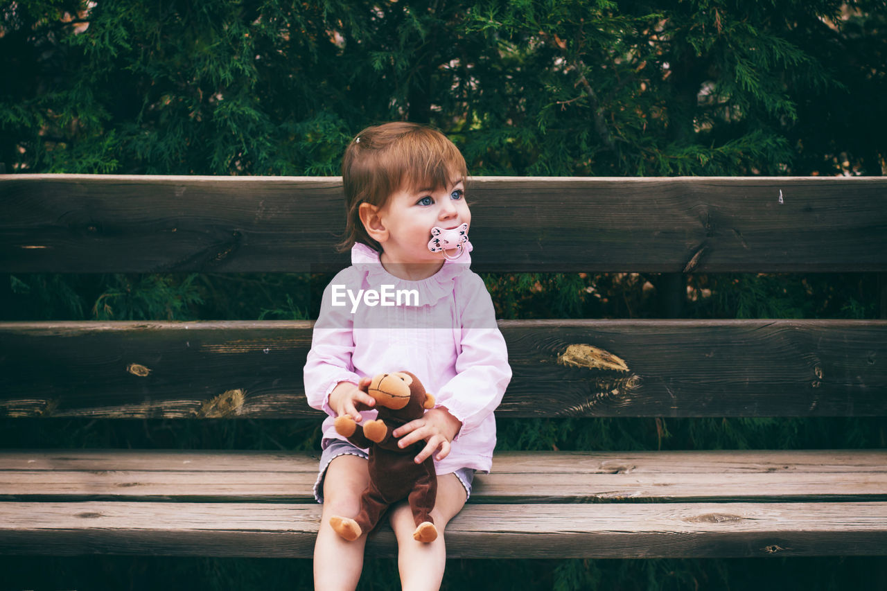 Cute baby girl holding stuffed toy while sitting at park