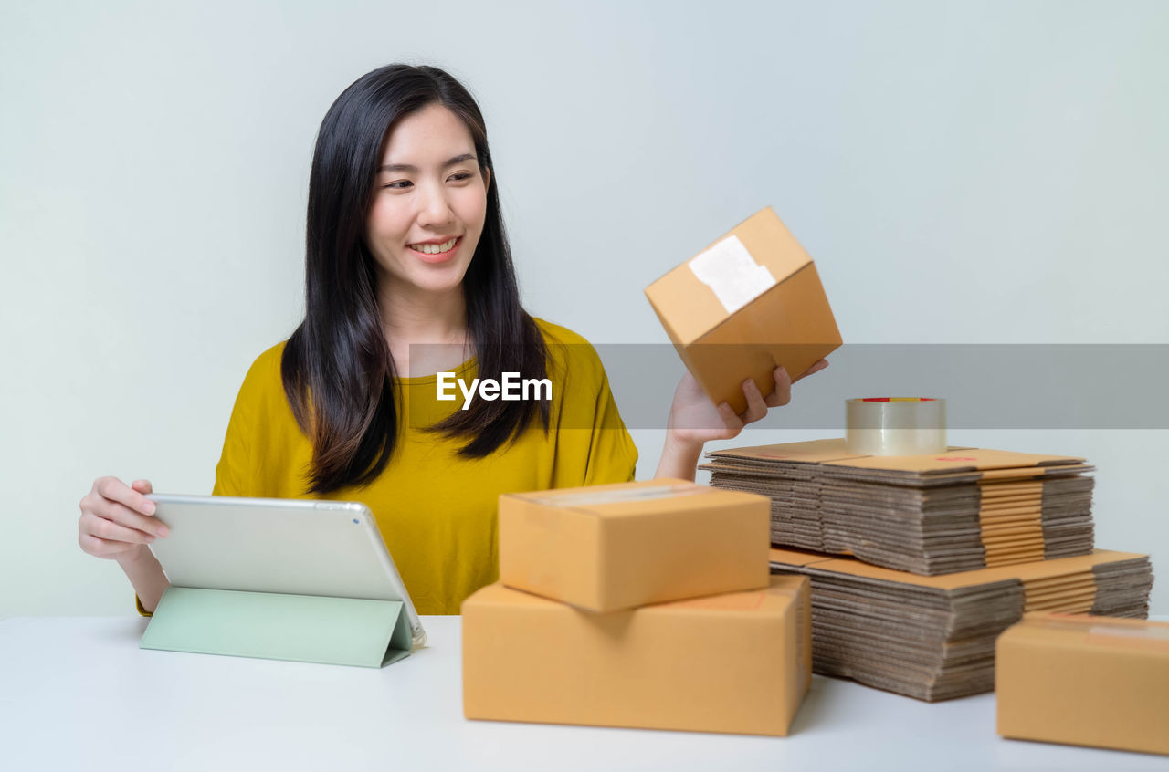 PORTRAIT OF A SMILING YOUNG WOMAN USING MOBILE PHONE IN BOX