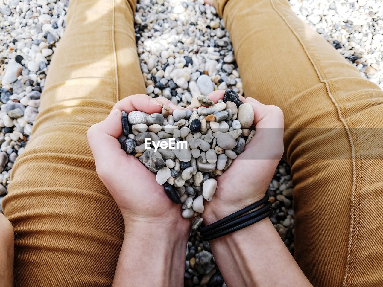 Cropped image of man holding pebbles while sitting at beach