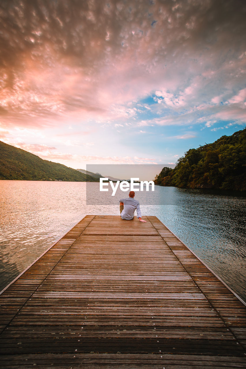 Man on pier over lake against sky during sunset