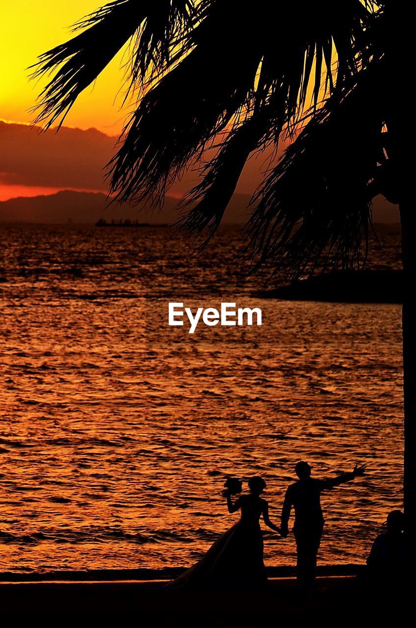 Silhouette couple standing at beach during sunset