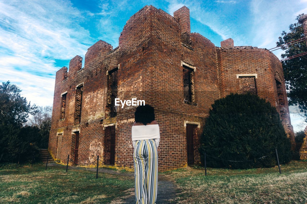 Rear view of woman looking at old building against sky