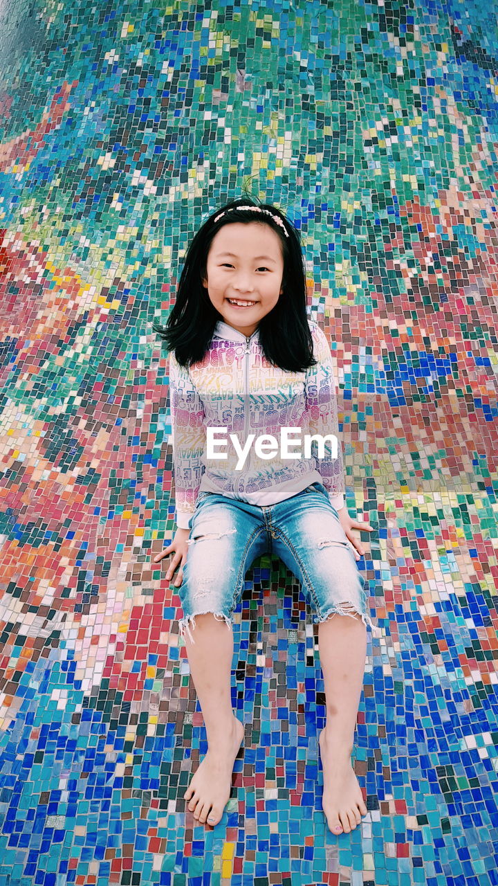 Portrait of smiling girl sitting on mosaic floor