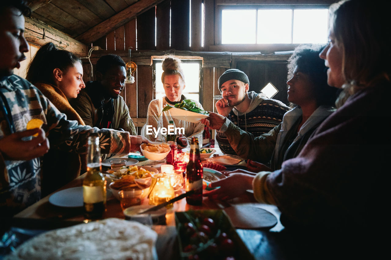 Male and female friends talking while having meal in cottage during weekend