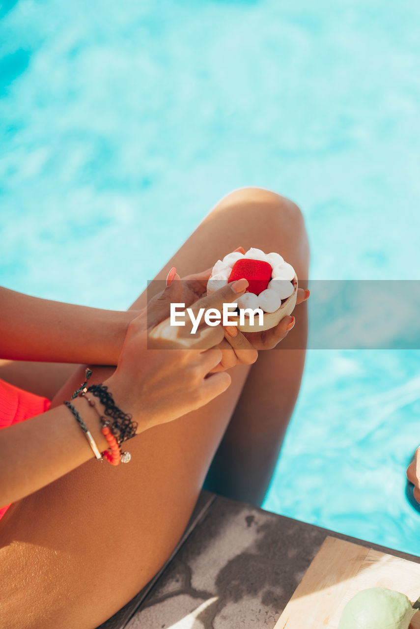 A young attractive girl holds a cake by the pool