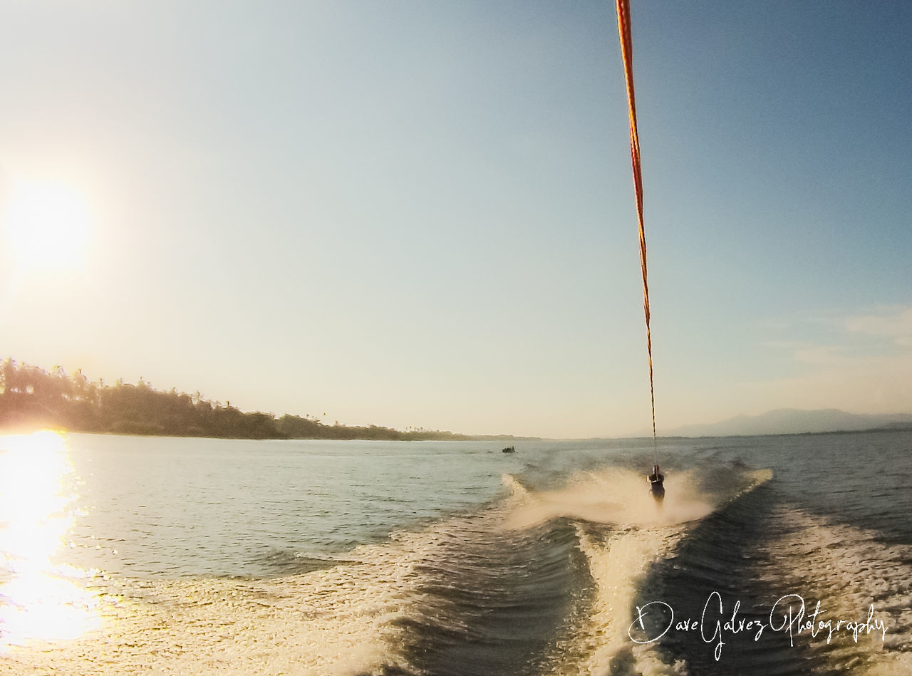 sky, water, sea, nature, sunlight, land, beauty in nature, wave, beach, sunset, scenics - nature, horizon, motion, shore, tranquility, ocean, outdoors, sports, day, clear sky, coast, wind, sun, tranquil scene, body of water, transportation, sunny, lens flare, copy space, nautical vessel, holiday