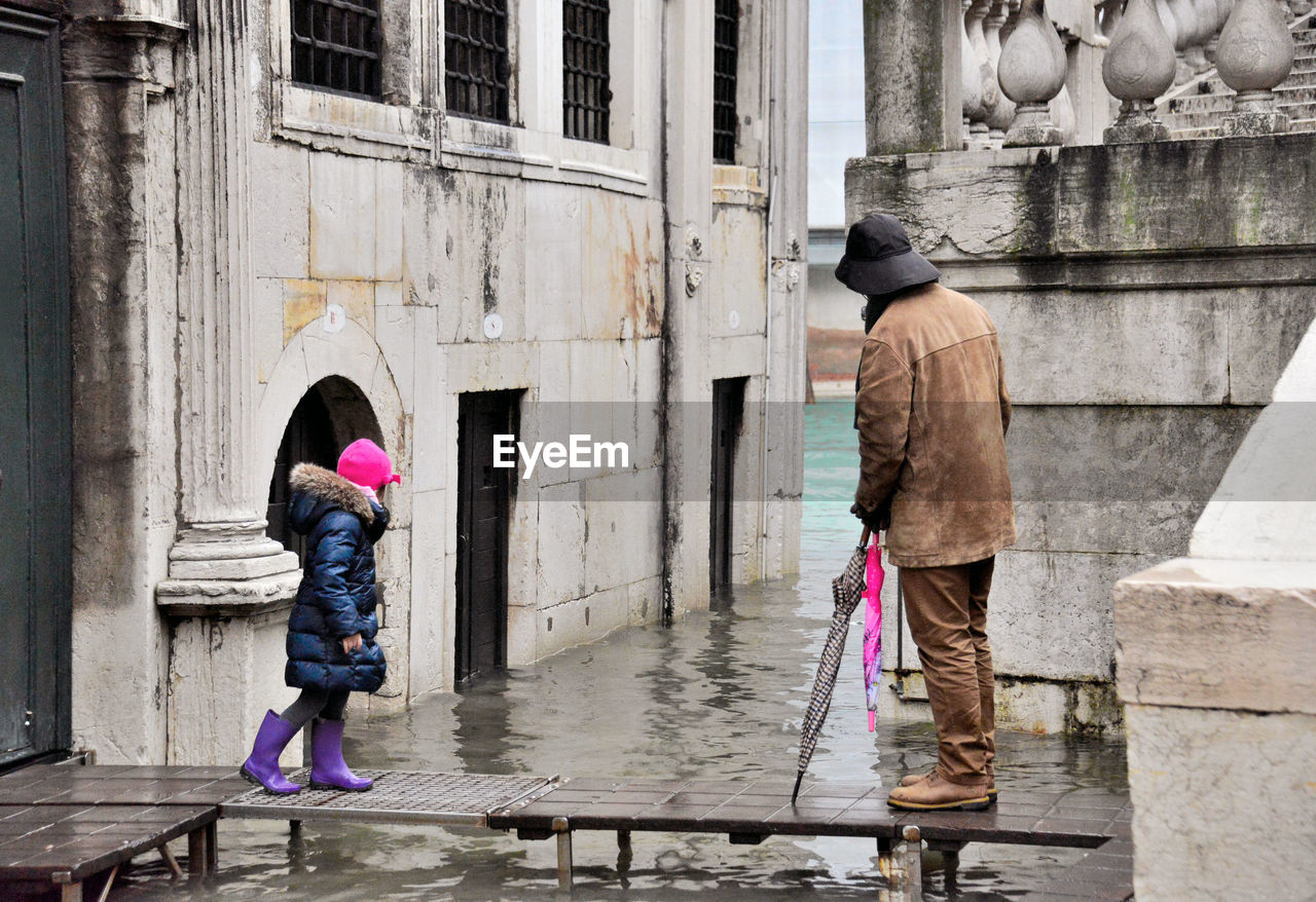 FULL LENGTH OF WOMAN WITH UMBRELLA STANDING BY BUILDING