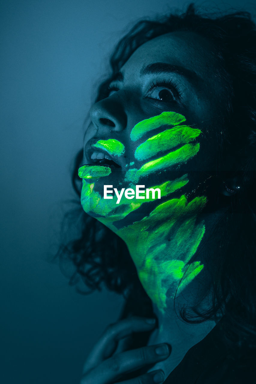 Woman with neon face paint against black background