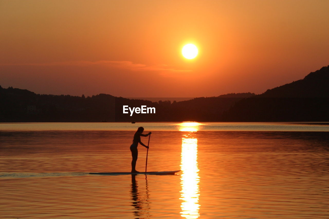 Silhouette woman in lake against orange sky
