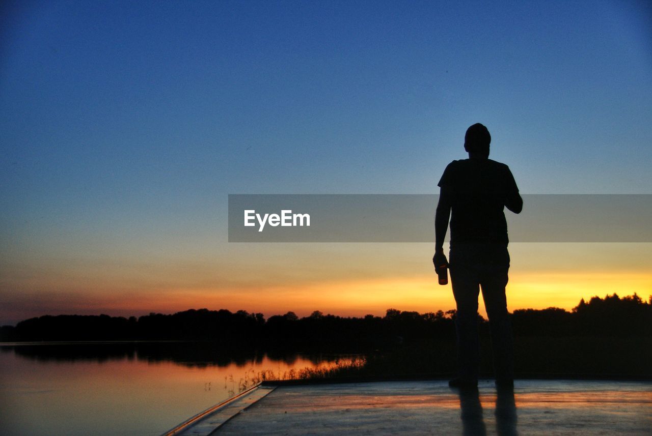 SILHOUETTE MAN STANDING ON JETTY AGAINST CLEAR SKY