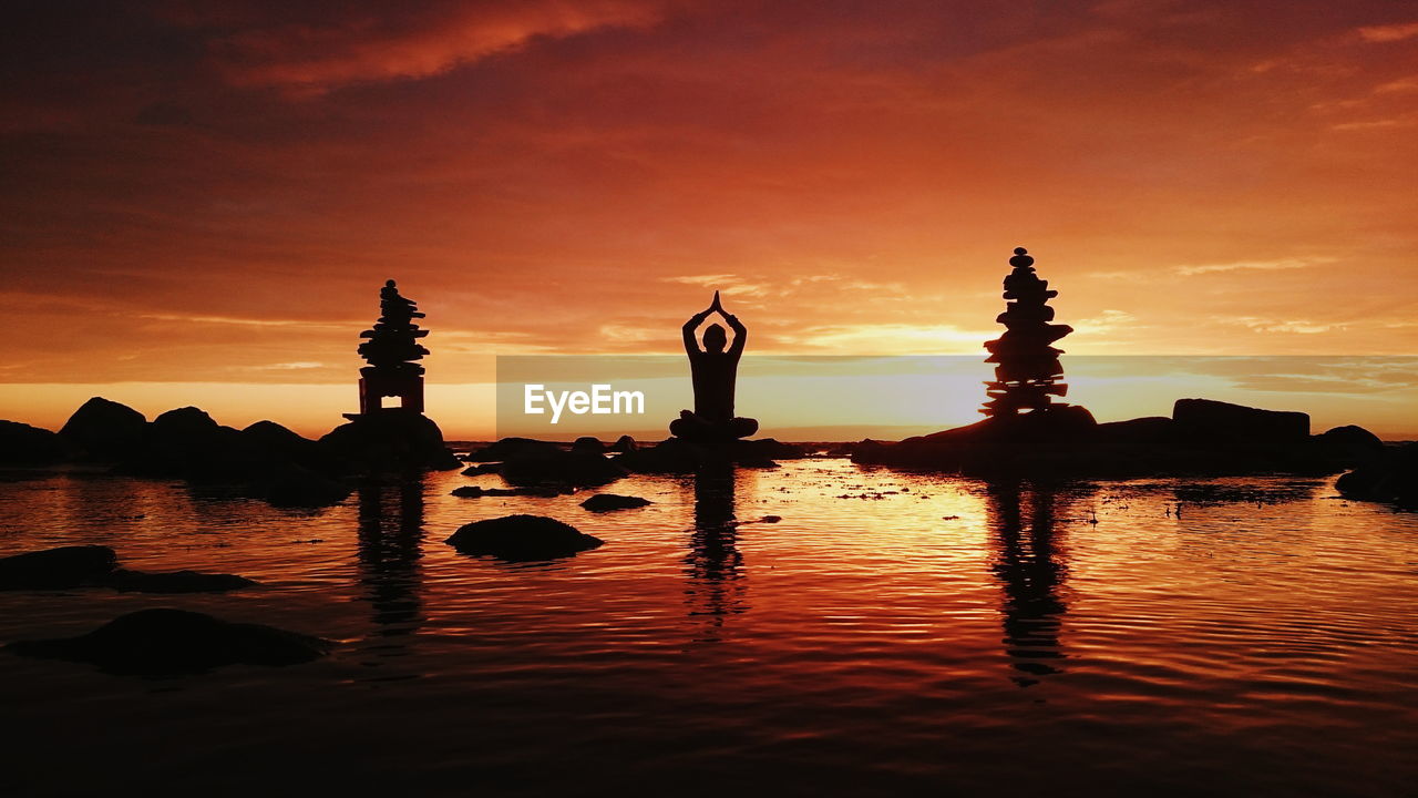 Silhouette person doing yoga at sea against sky during sunset