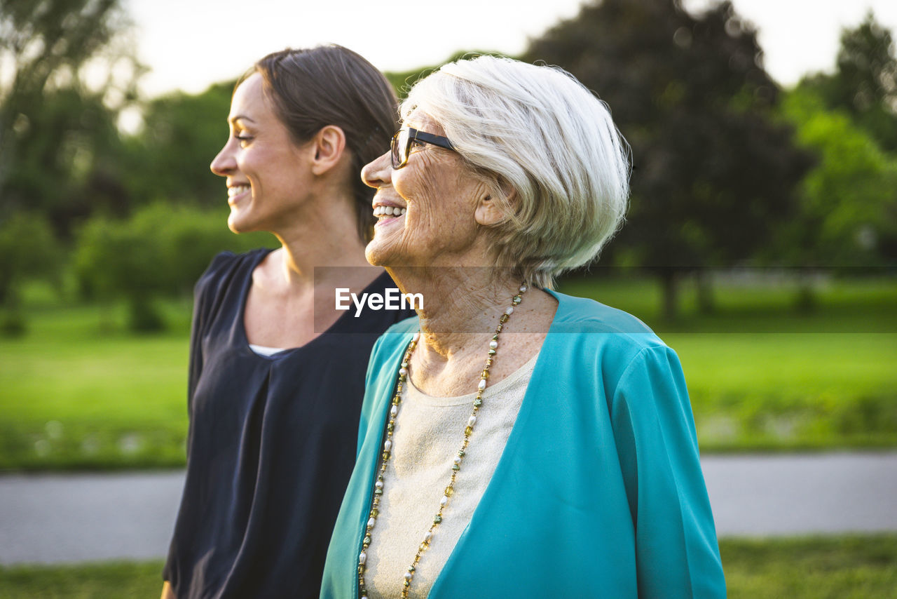 Smiling grandmother looking away while standing by granddaughter at park