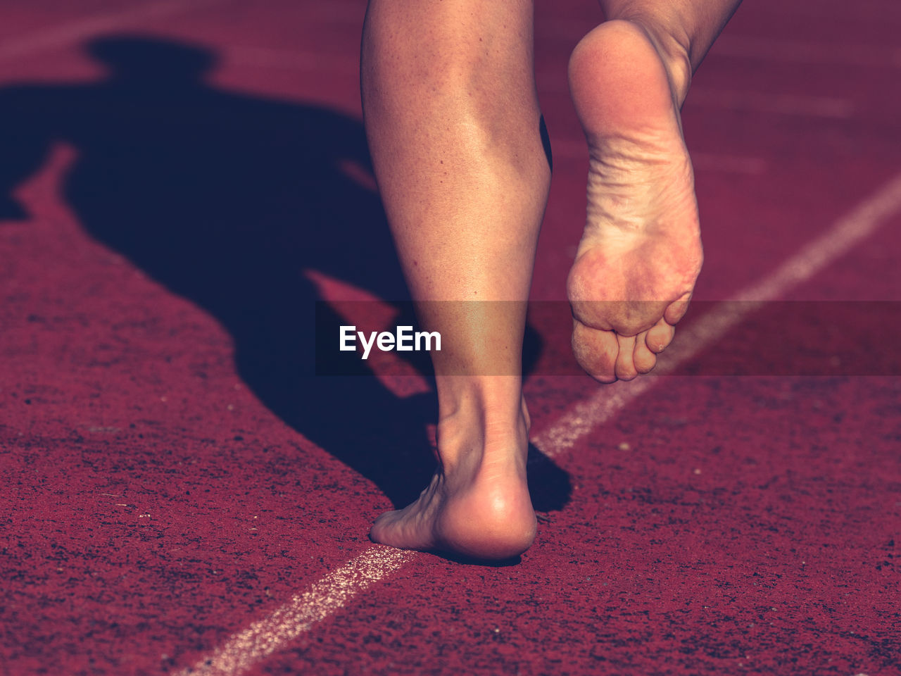 Solid bare feet of hard training woman. a woman runs along soft surface of a running track in pants