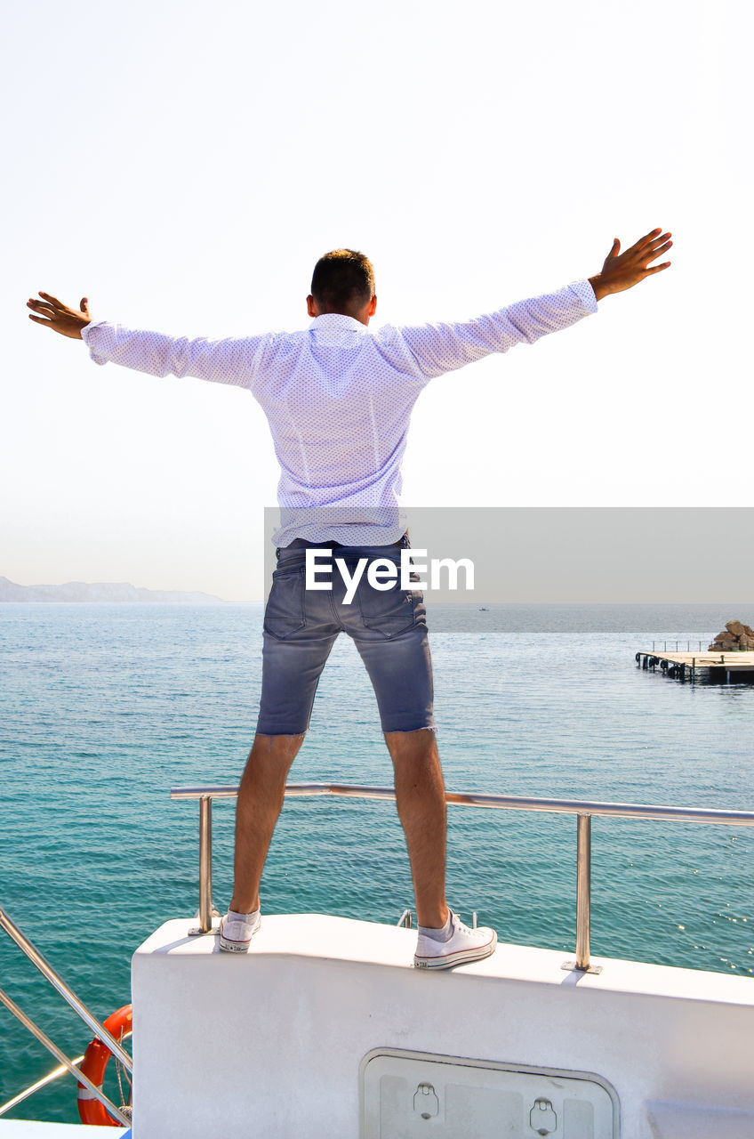 Rear view of man standing on boat in sea against sky