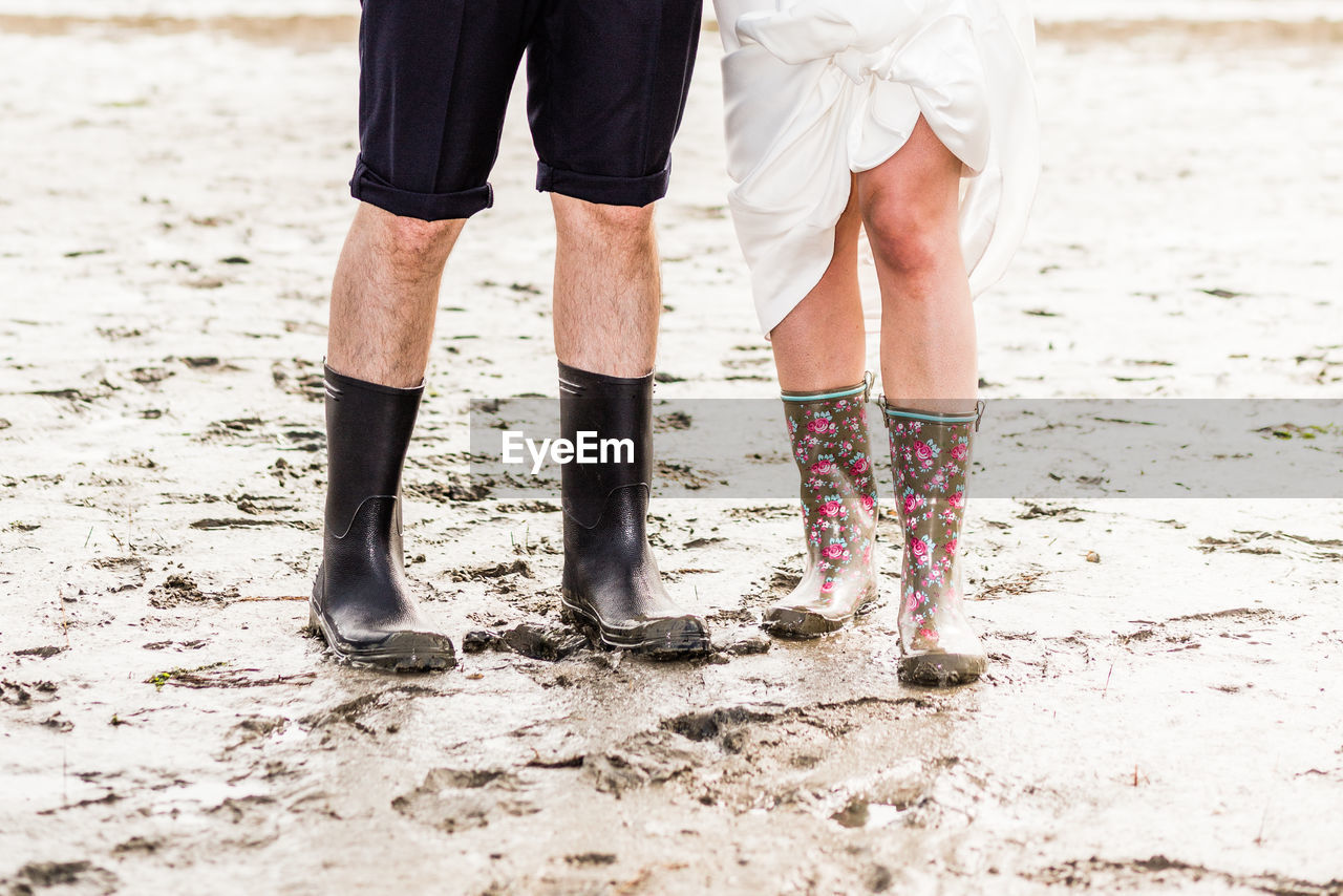 Low section of man and woman wearing rubber boots while standing mud