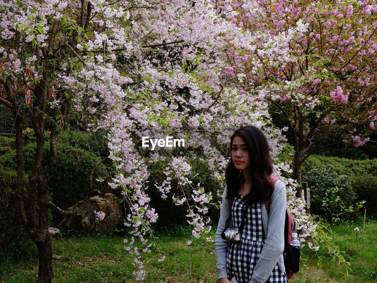 Portrait of beautiful woman standing by flower tree