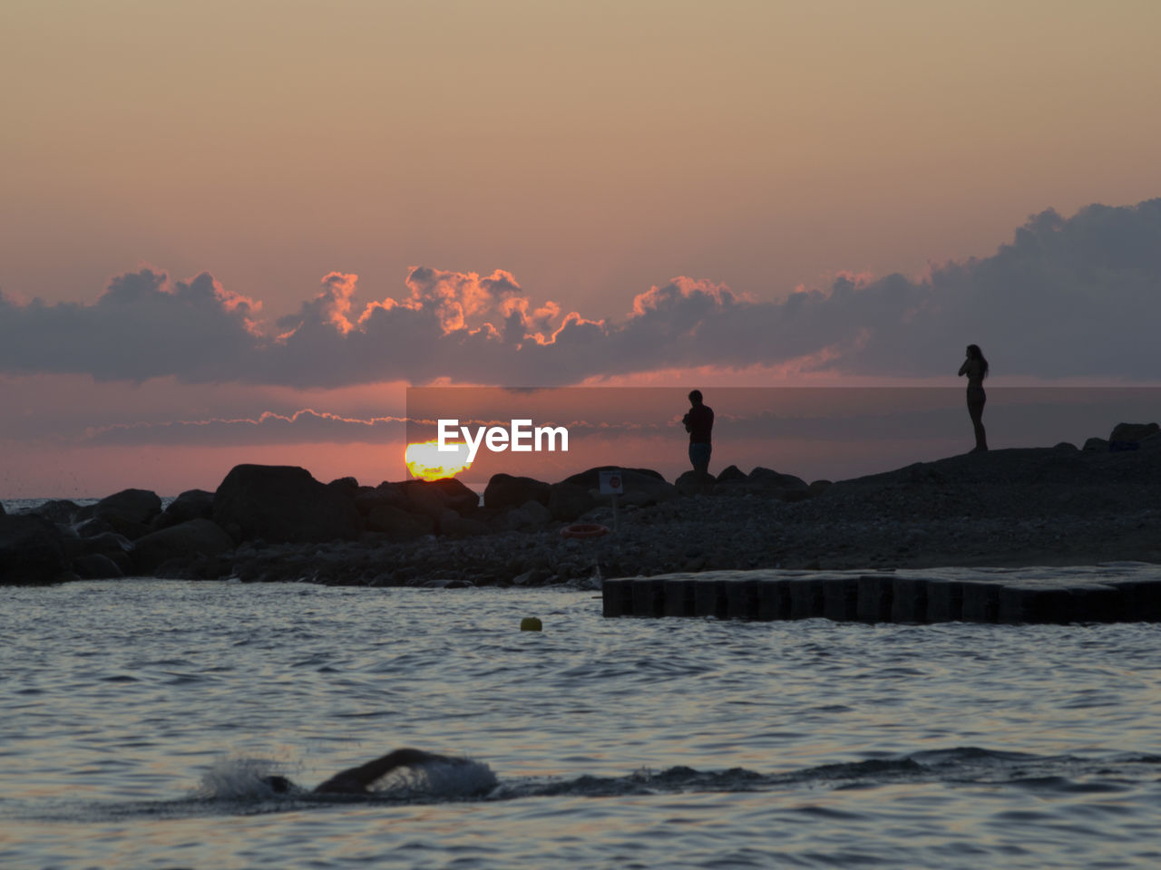 Silhouette people at beach against sky during sunset