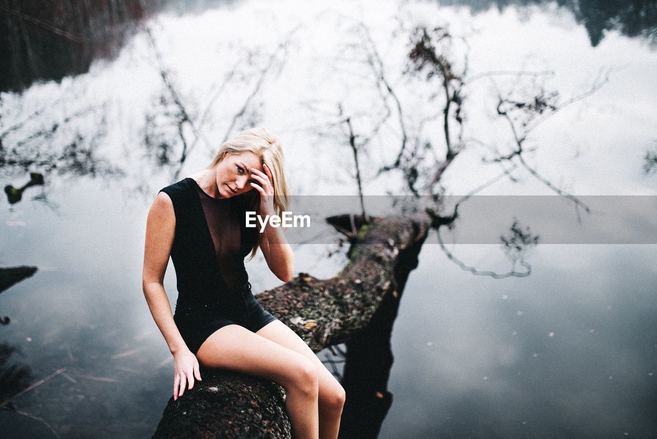 Portrait of woman with hand in hair sitting on fallen tree over lake