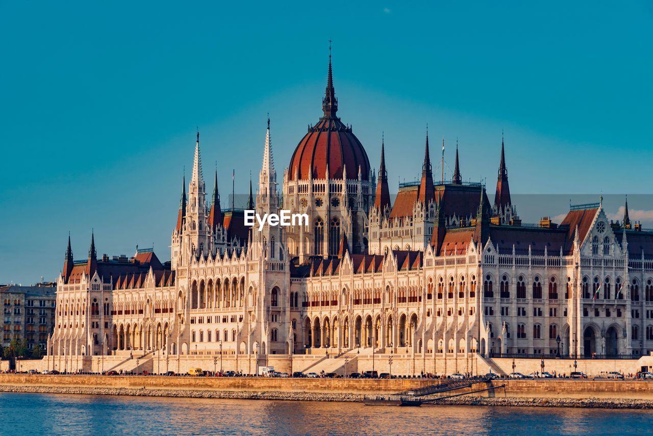 Hungarian parliament building by river against blue sky