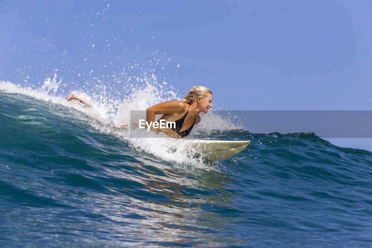 Confident woman surfing in sea against sky