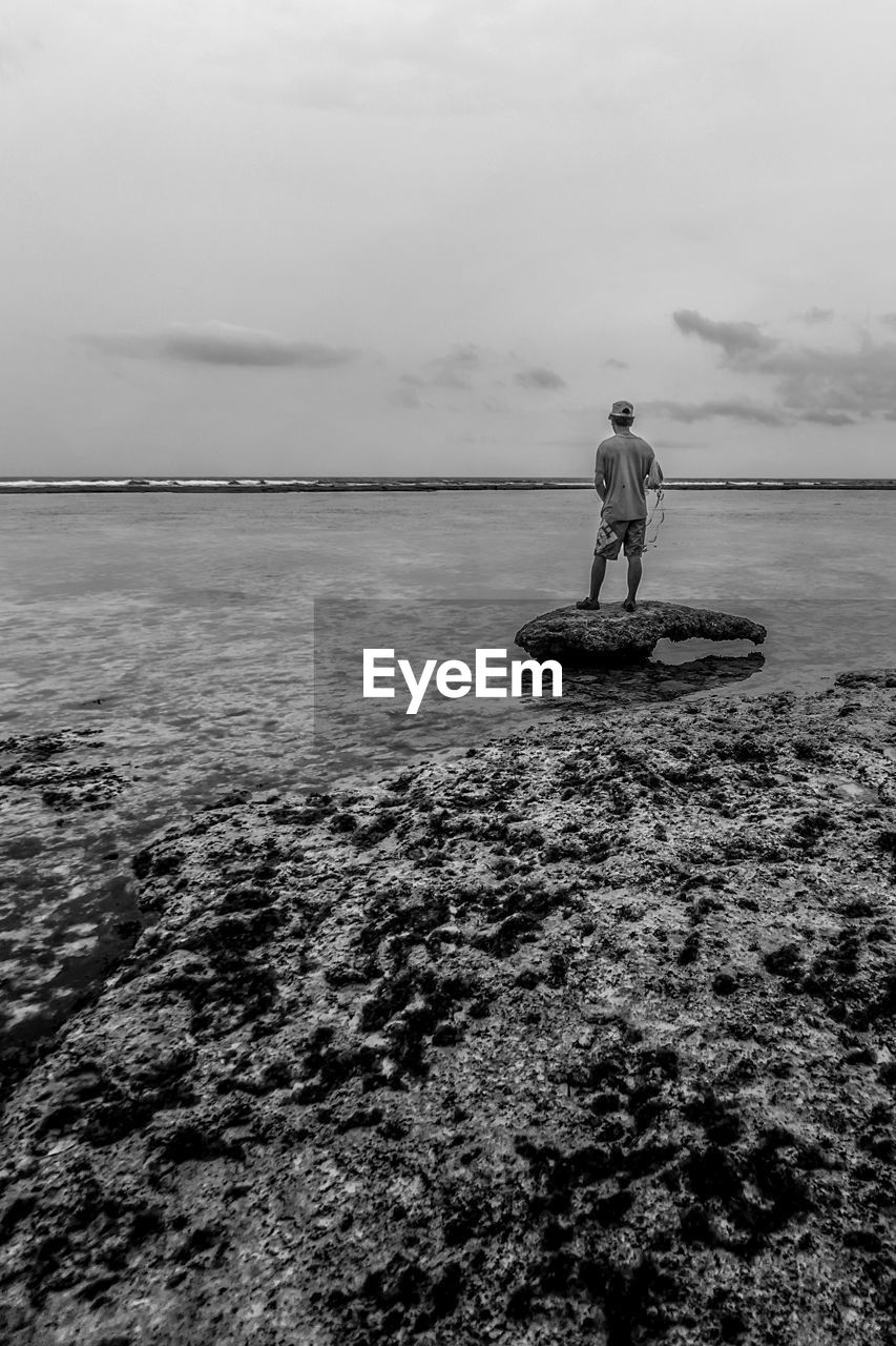 REAR VIEW OF MAN STANDING ON SEA SHORE