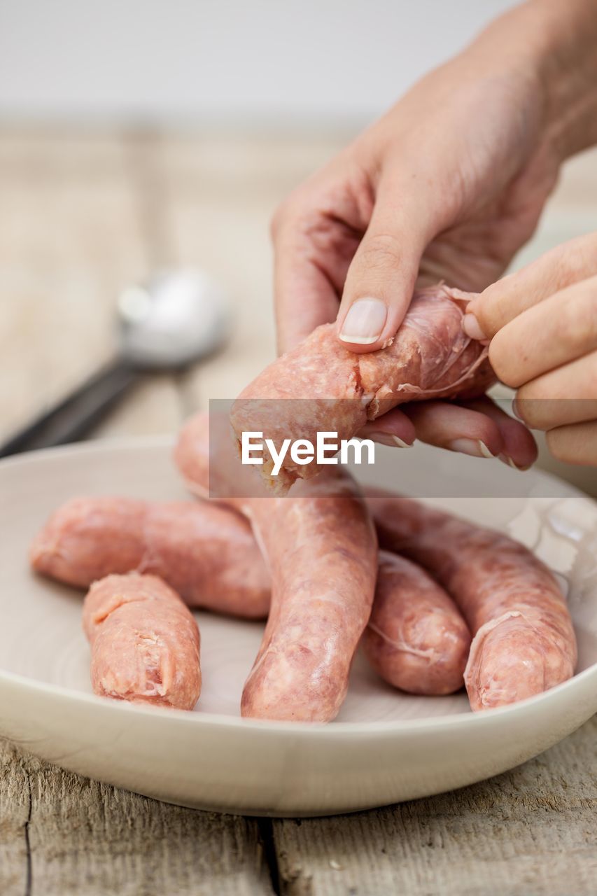 Cropped image of hand holding peeling sausage in bowl