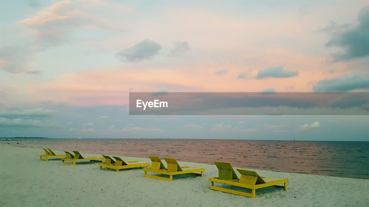 Lounge chairs on sea shore against sky during sunset