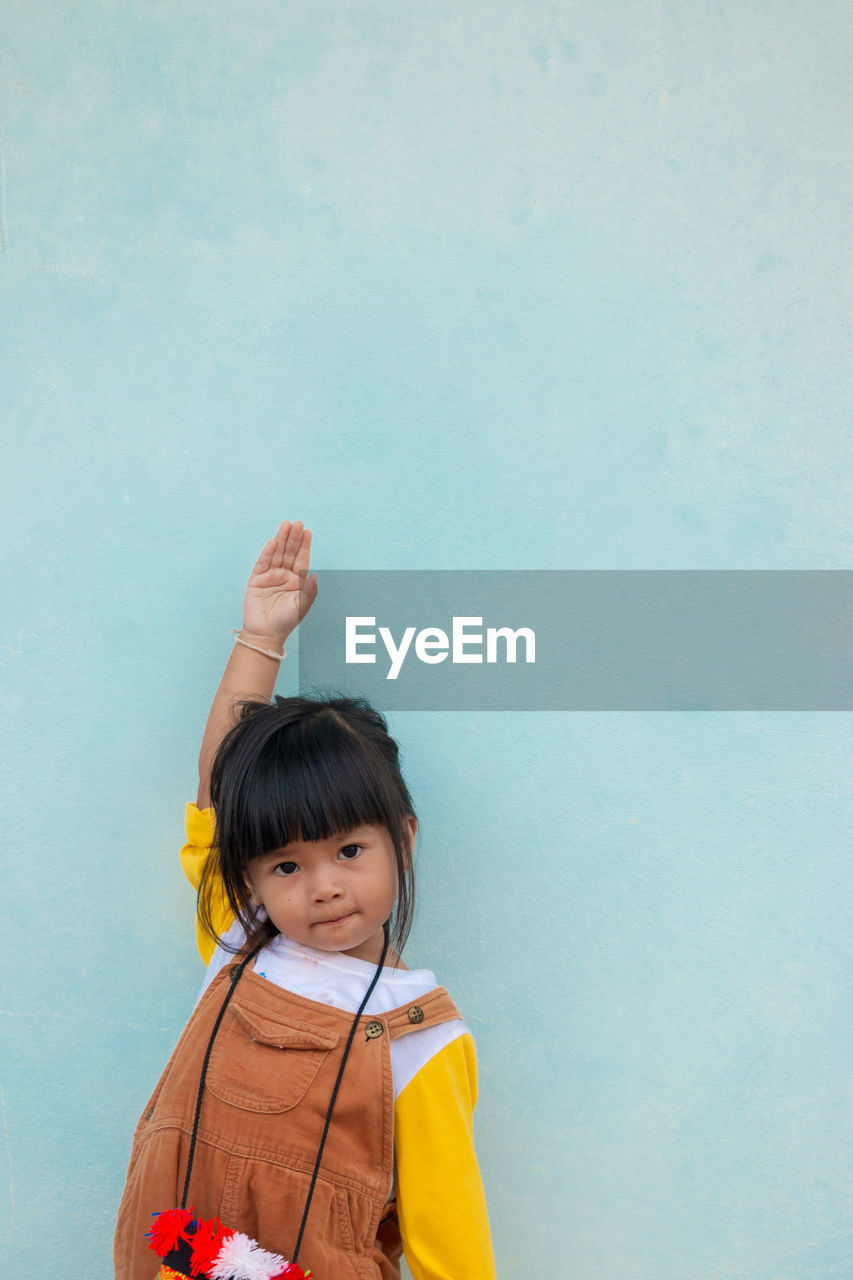 Portrait of cute baby girl with hand raised standing against wall