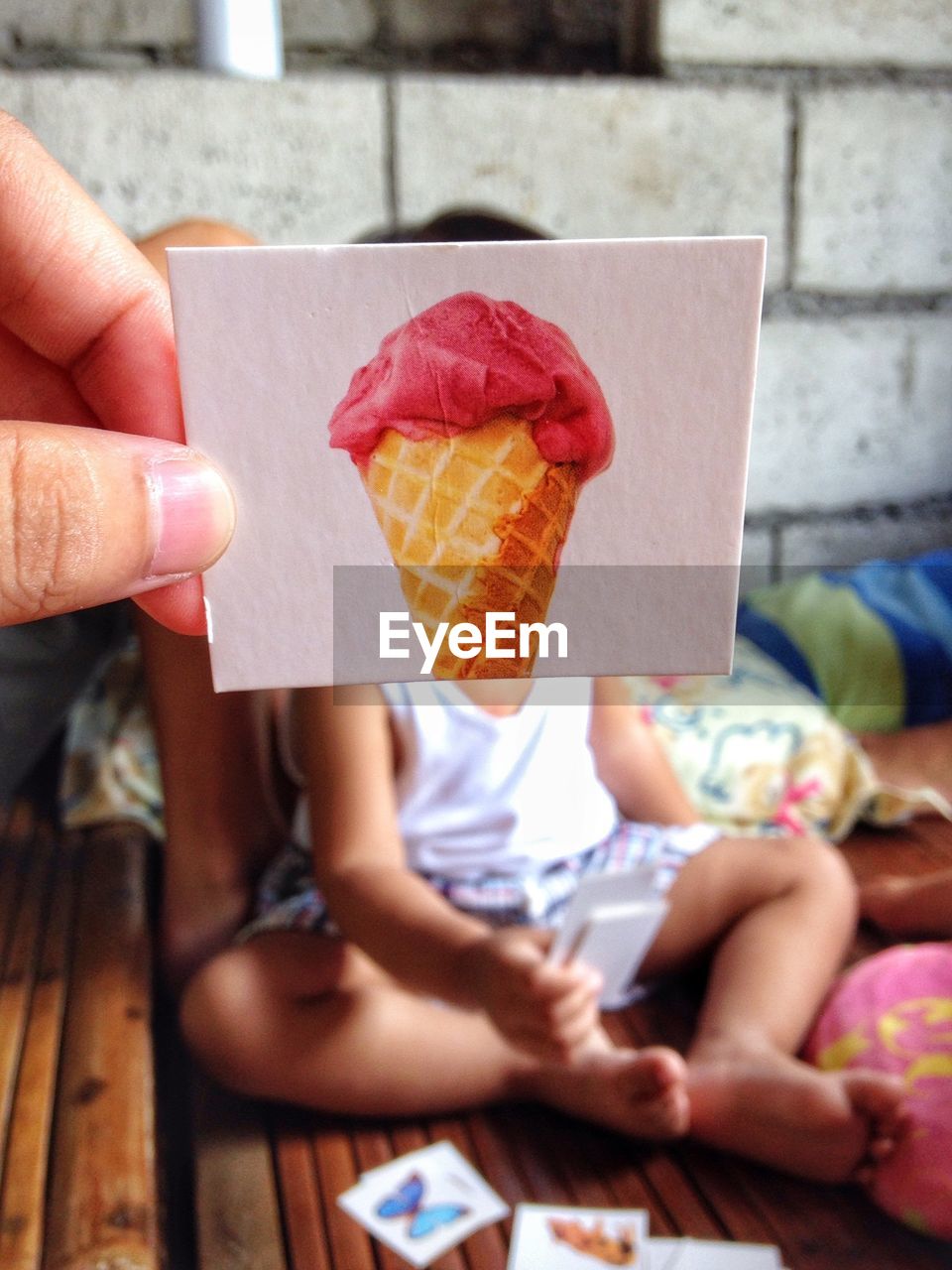 Cropped hand holding ice cream photograph against child