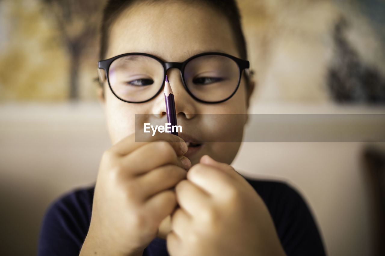 Smart young asian boy wearing glasses squints at the pencil. the vision diseases problem.