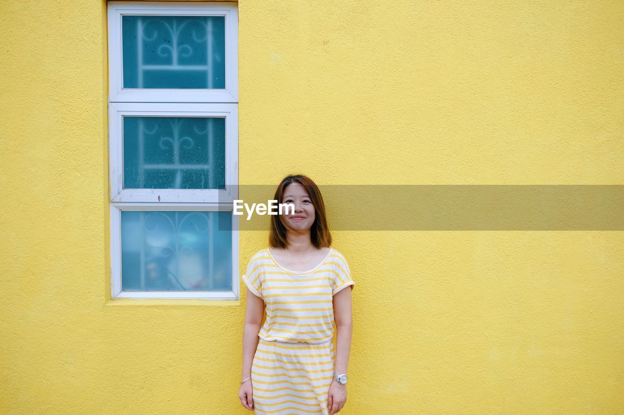 Portrait of smiling woman standing against yellow wall