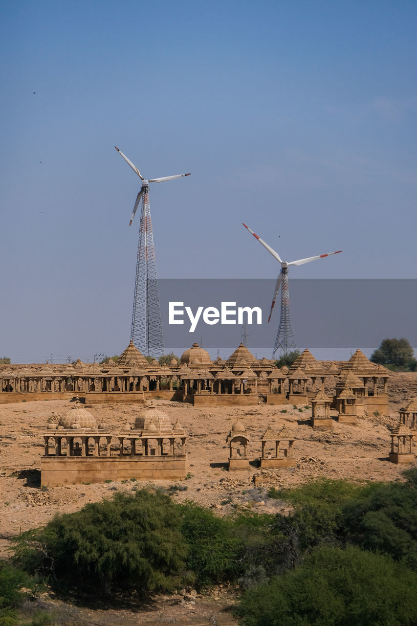 View of wind turbines behind ruins of bada bagh against sky