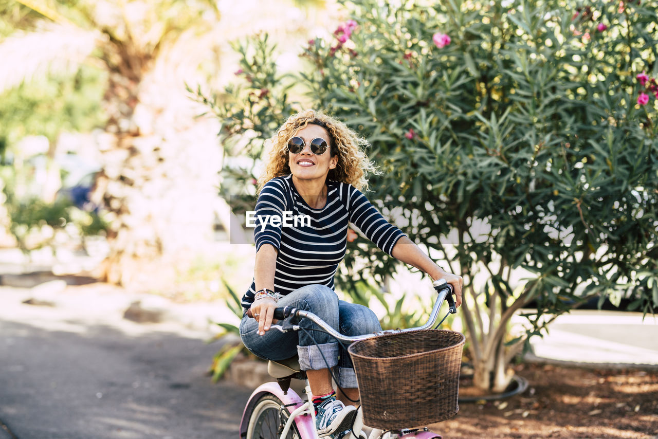 Smiling young woman riding bicycle against tree