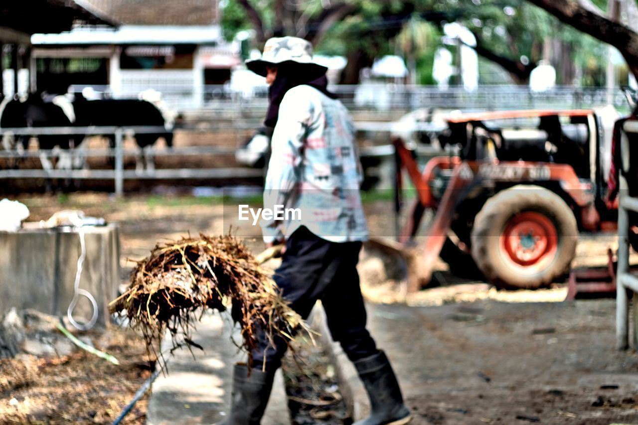 Side view full length of farmer holding fork with straw at farm