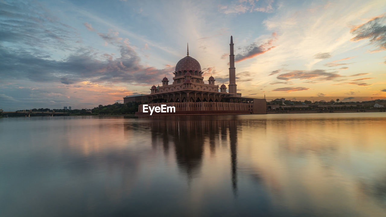 View of mosque by lake against sky at sunset