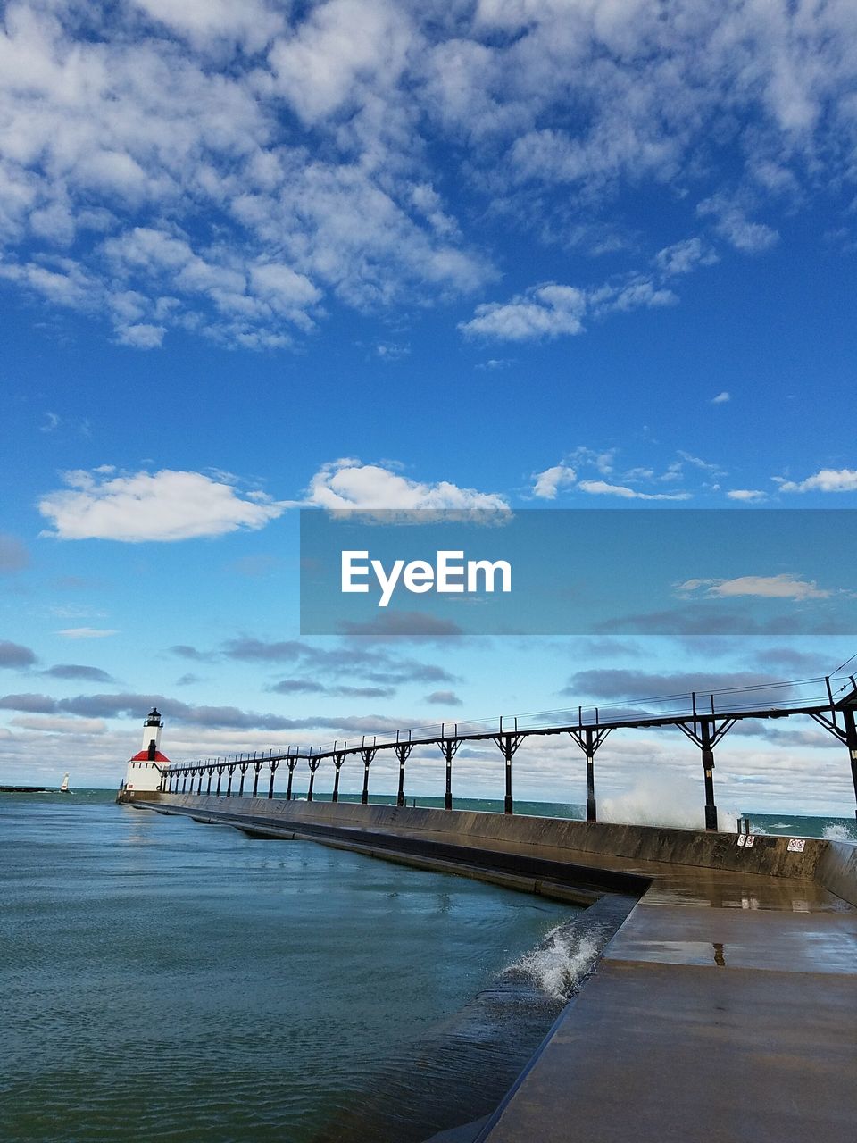 Lighthouse on pier over sea against sky