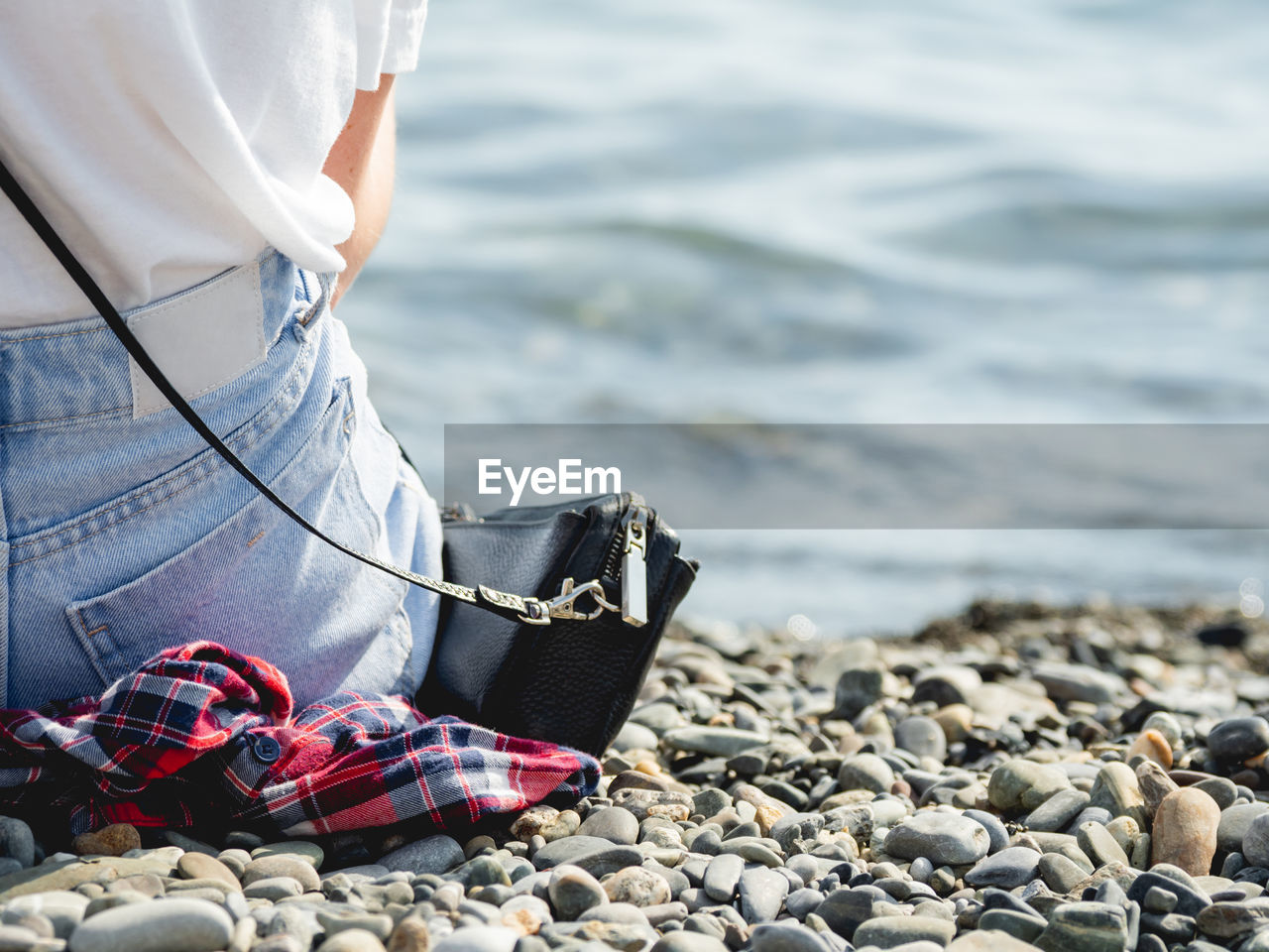 Woman in jeans sits on pebble beach. rear view of woman at seaside. long awaited vacations.