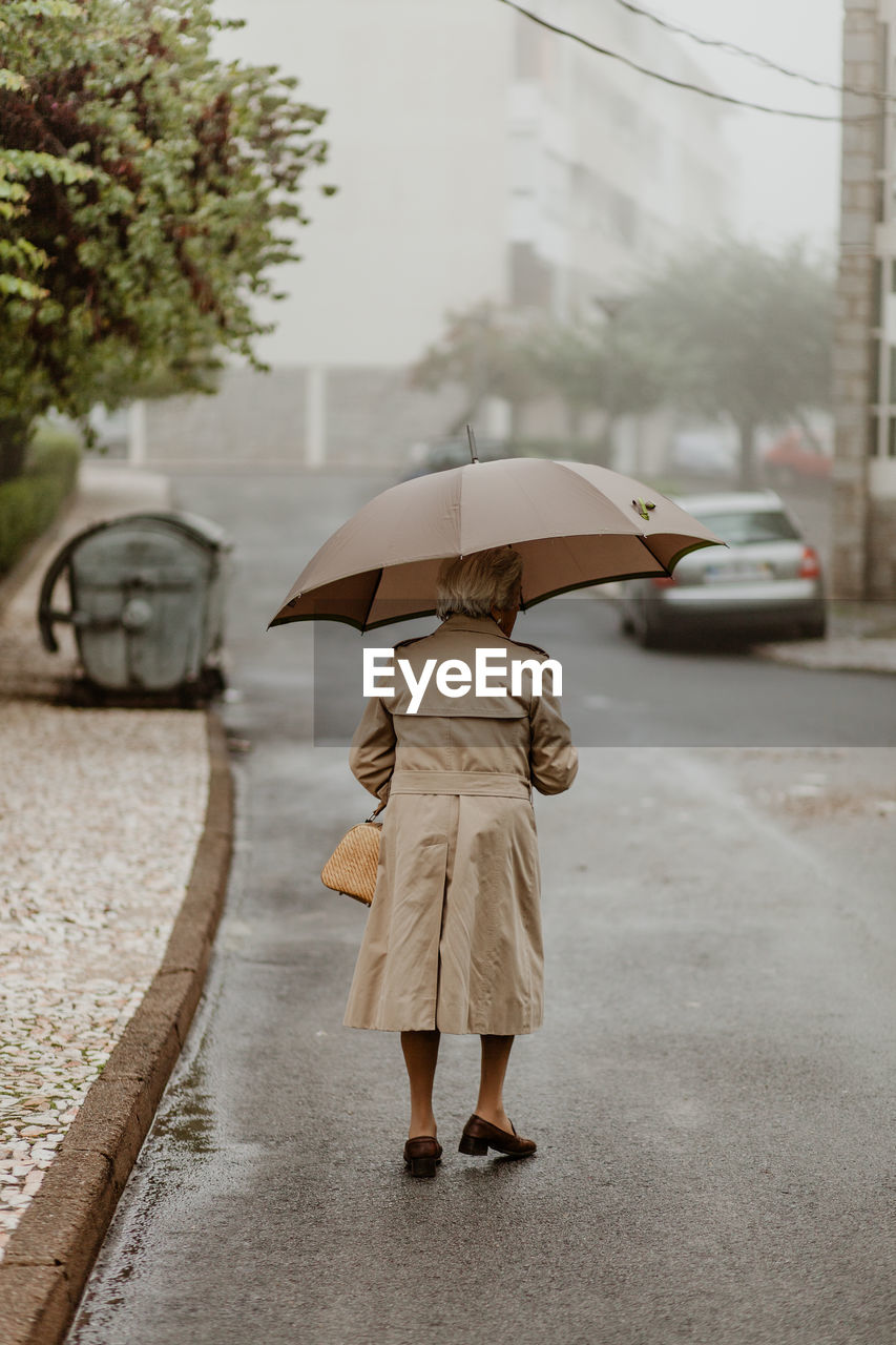 Rear view of woman walking on wet street during rainy season