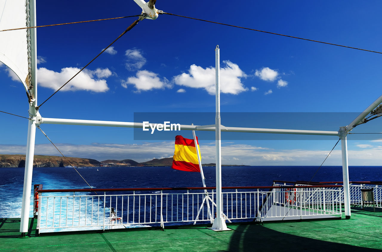 Ferry boat with spain flag in sea against cloudy sky
