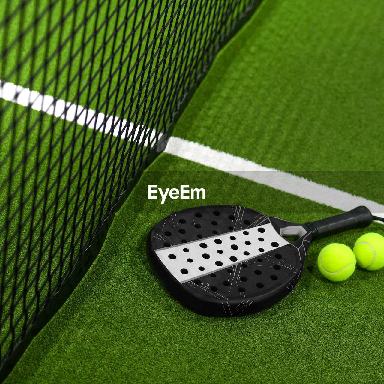 Closeup view of  paddle racket and balls in a padel tennis court near the net green with white lines