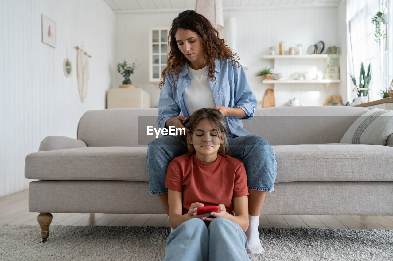 Mother braiding hair of teenage girl daughter at home, mom spending time with teen child