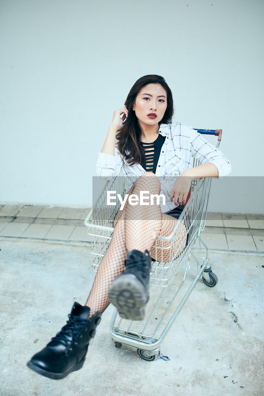 Portrait of young woman sitting in shopping cart