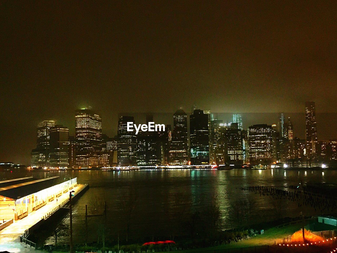 River by illuminated cityscape against sky at night