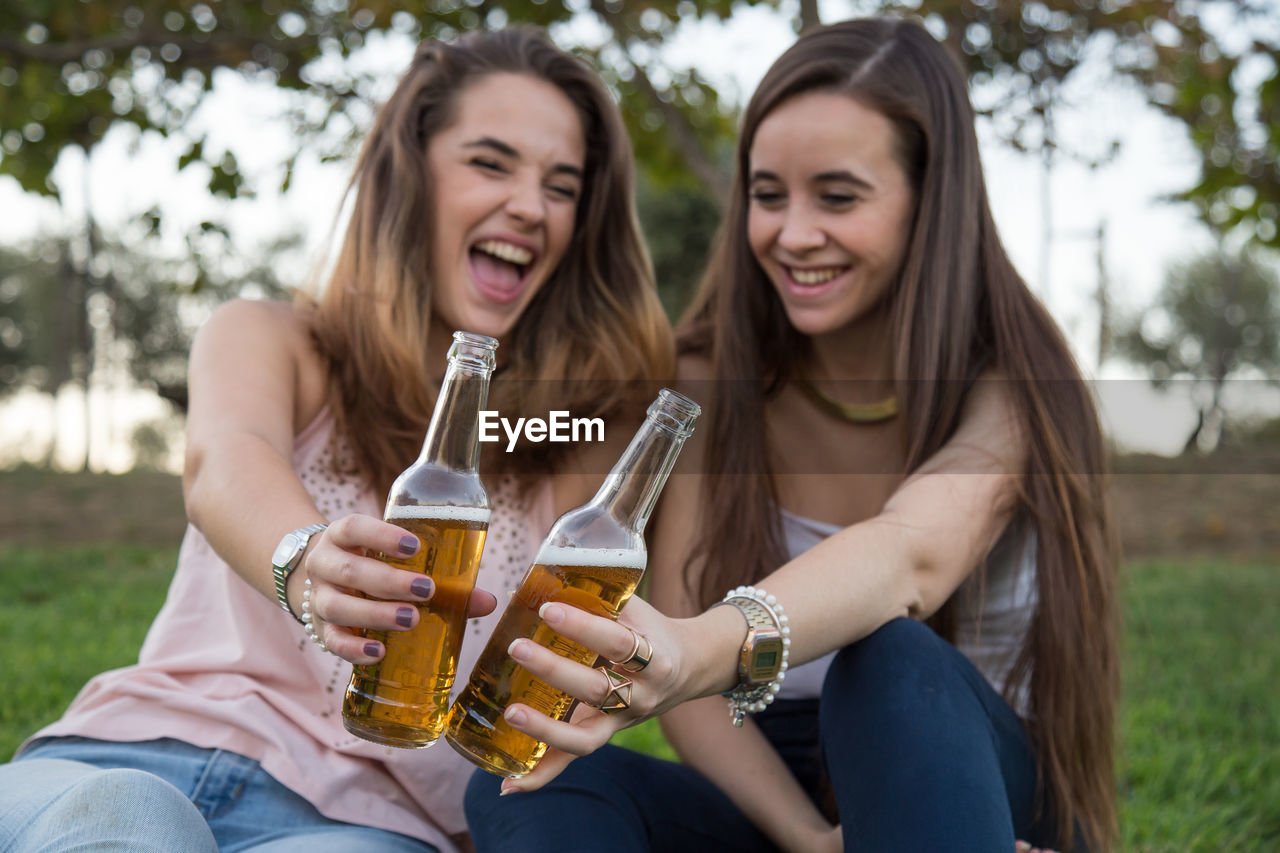 Happy friends enjoying beer while sitting on grass at park