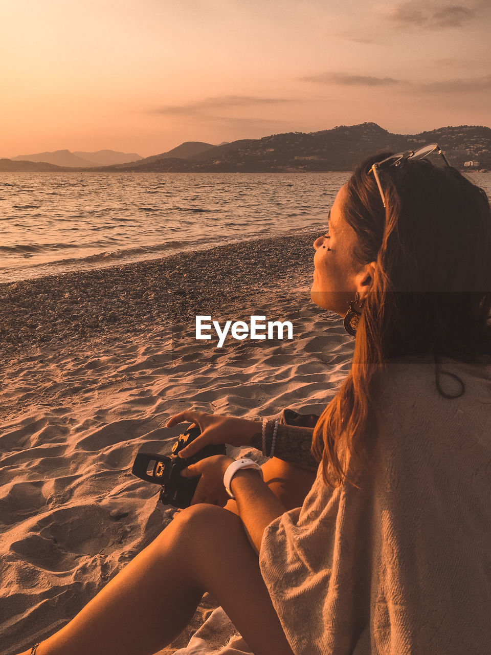 Woman relaxing on beach against sky during sunset