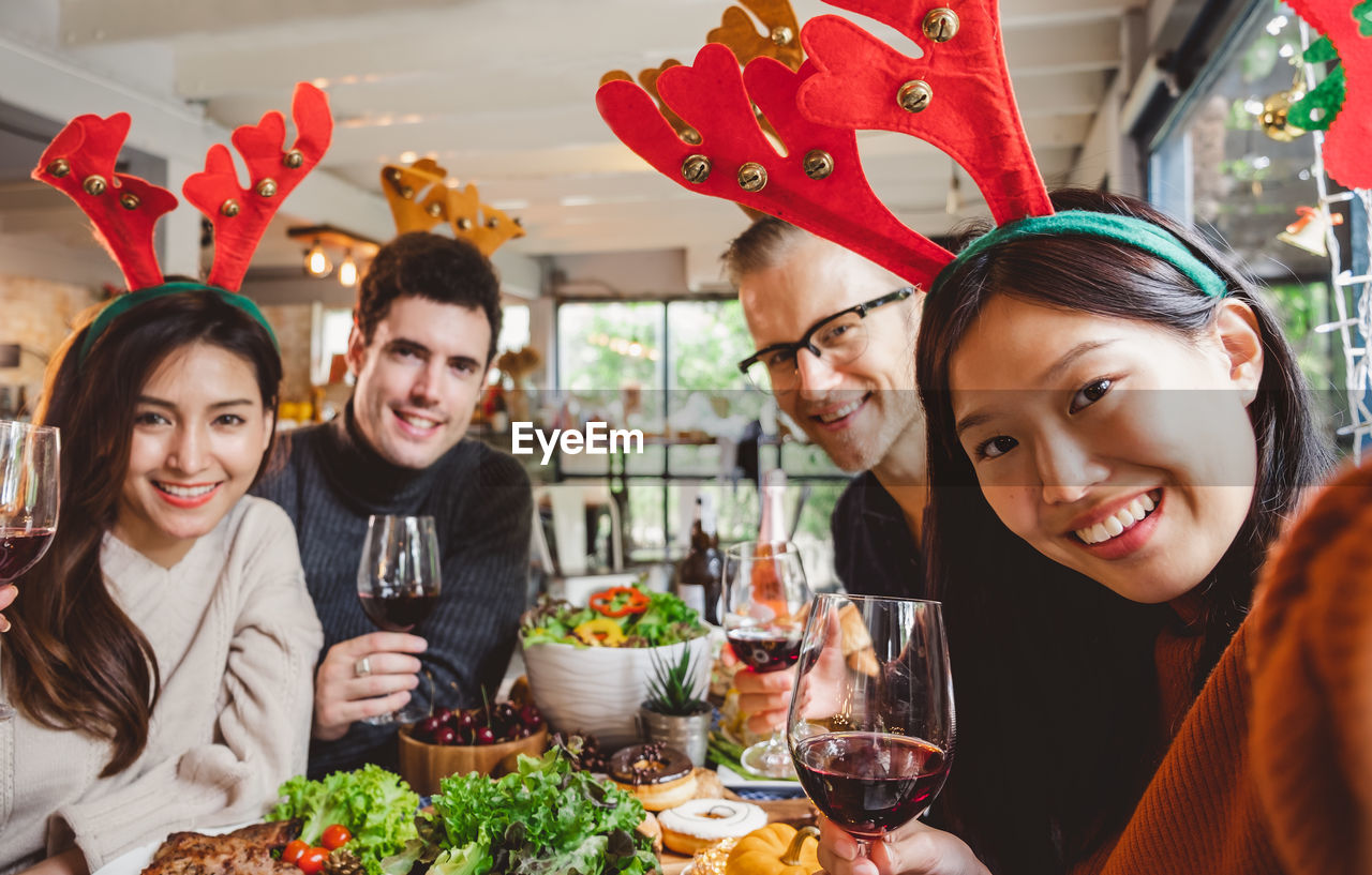 Portrait of happy friends with red wine in restaurant during christmas