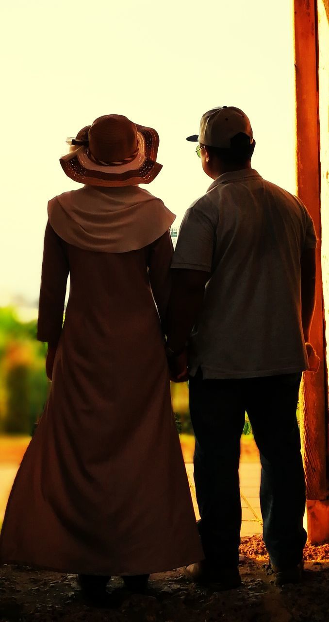 Rear view of couple holding hands while standing against clear sky