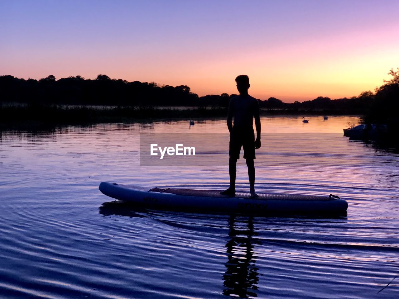 Boy standing over boat on lake against sky during sunset