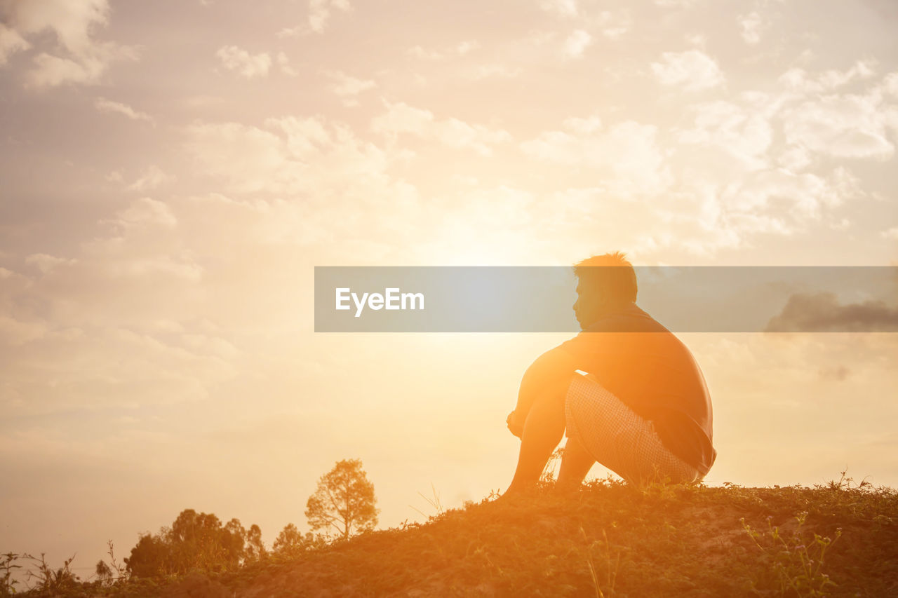 Low angle view of man sitting on land against sky during sunset