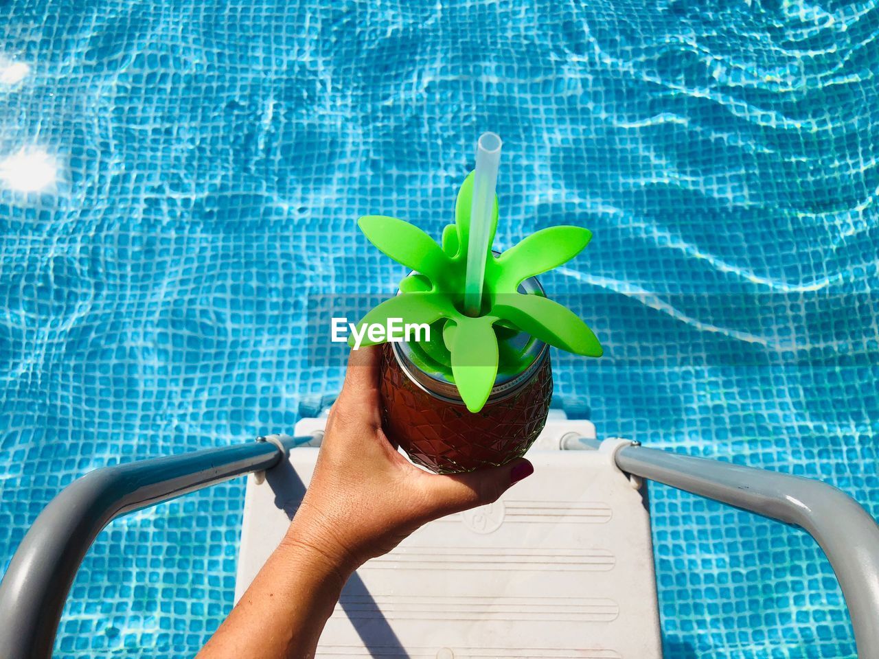 Cropped hand of woman holding drink over swimming pool